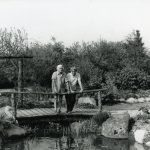 Jutta og Peter Ottesen, Bakkely stående ved rækværket på en bro over vandløbet fra en lille sø i deres smukke have.